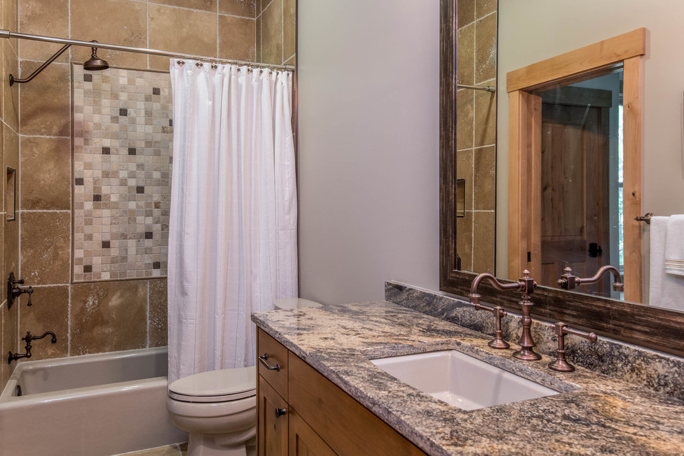 Inspiration for a mid-sized rustic 3/4 brown tile and travertine tile brown floor alcove bathtub remodel with recessed-panel cabinets, medium tone wood cabinets, gray walls, an undermount sink, granite countertops and multicolored countertops