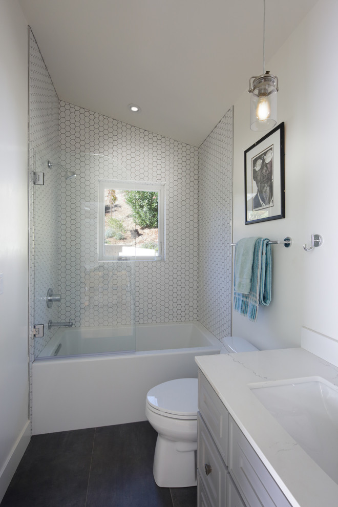 Photo of a small contemporary bathroom in Other with furniture-like cabinets, grey cabinets, an alcove tub, a shower/bathtub combo, a one-piece toilet, white tile, white walls, ceramic floors, an undermount sink, marble benchtops, grey floor, a hinged shower door, white benchtops, a single vanity, a freestanding vanity and vaulted.