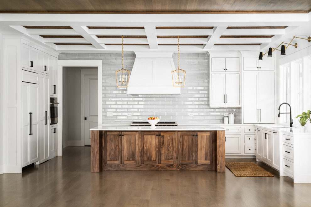 Photo of a country kitchen in Chicago with an undermount sink, shaker cabinets, white cabinets, white splashback, subway tile splashback, panelled appliances, dark hardwood floors, with island, brown floor, white benchtop and coffered.