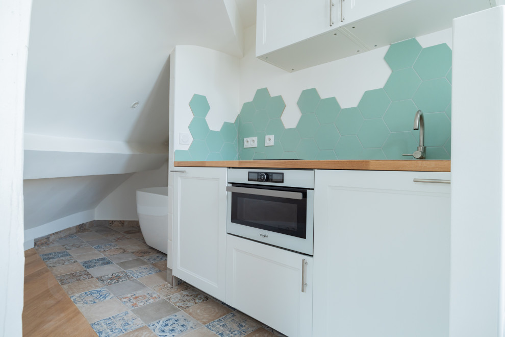 Inredning av ett skandinaviskt litet brun linjärt brunt kök med öppen planlösning, med en undermonterad diskho, träbänkskiva, grönt stänkskydd, stänkskydd i keramik, vita vitvaror, cementgolv och blått golv