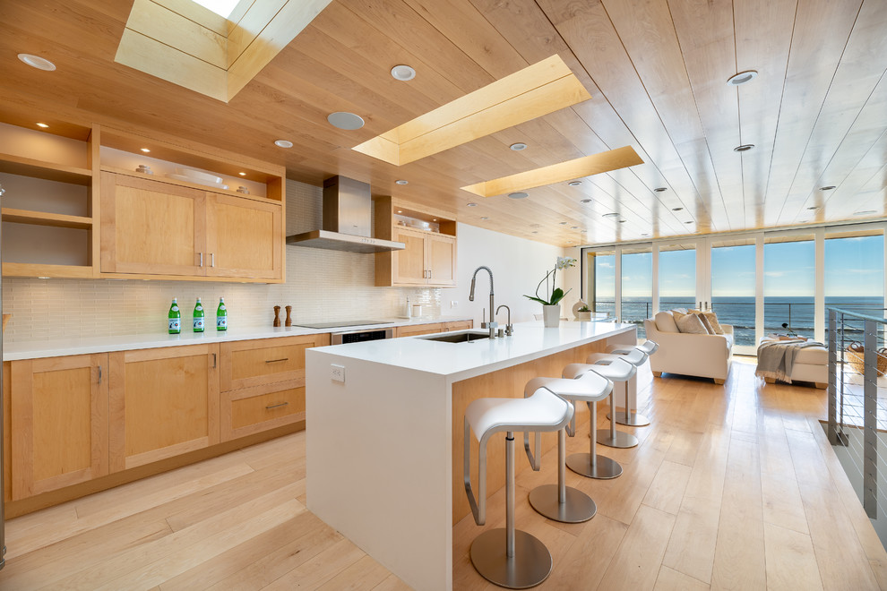 Expansive contemporary galley open plan kitchen in Los Angeles with a single-bowl sink, shaker cabinets, light wood cabinets, quartz benchtops, beige splashback, glass tile splashback, stainless steel appliances, light hardwood floors, with island, yellow floor and white benchtop.
