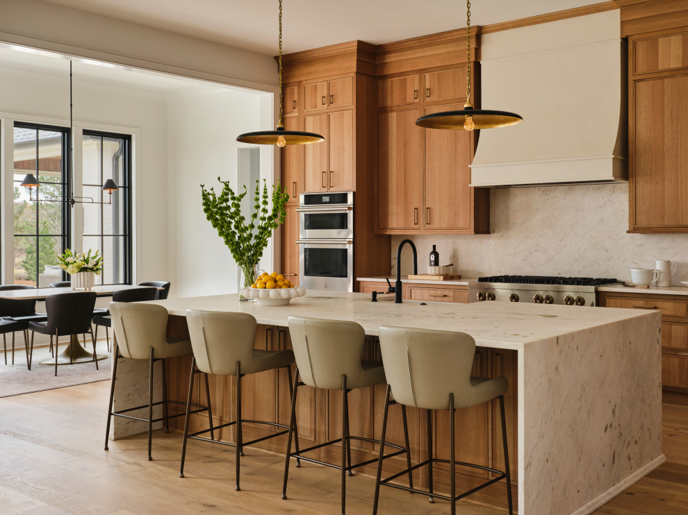 Inspiration for a transitional galley medium tone wood floor and brown floor kitchen remodel with a farmhouse sink, shaker cabinets, medium tone wood cabinets, white backsplash, stone slab backsplash, stainless steel appliances, an island and white countertops
