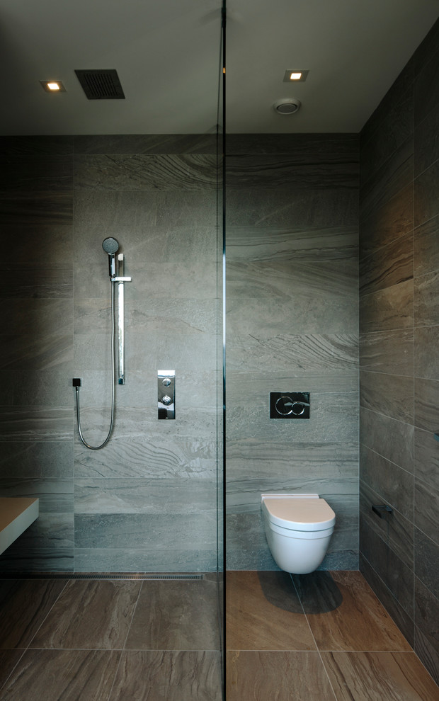 Inspiration for a large contemporary master bathroom in Vancouver with flat-panel cabinets, medium wood cabinets, a freestanding tub, a curbless shower, a wall-mount toilet, gray tile, porcelain tile, grey walls, porcelain floors, a vessel sink, engineered quartz benchtops, grey floor, a hinged shower door and white benchtops.