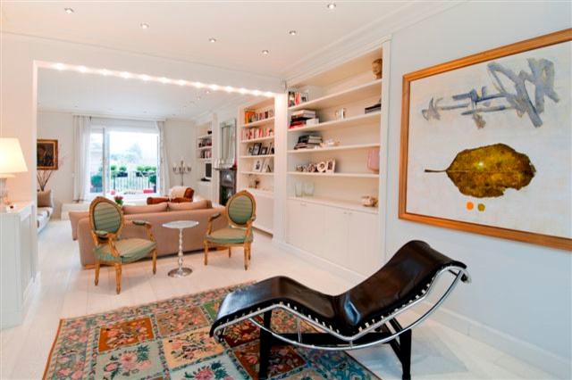Photo of an expansive eclectic open concept living room in London with a library, white walls, painted wood floors, a standard fireplace, a metal fireplace surround and no tv.