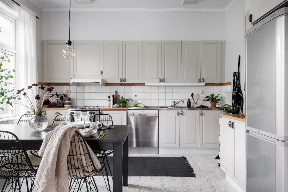 Inspiration for a mid-sized scandinavian l-shaped eat-in kitchen in Gothenburg with an integrated sink, raised-panel cabinets, grey cabinets, white splashback, stainless steel appliances, no island and wood benchtops.