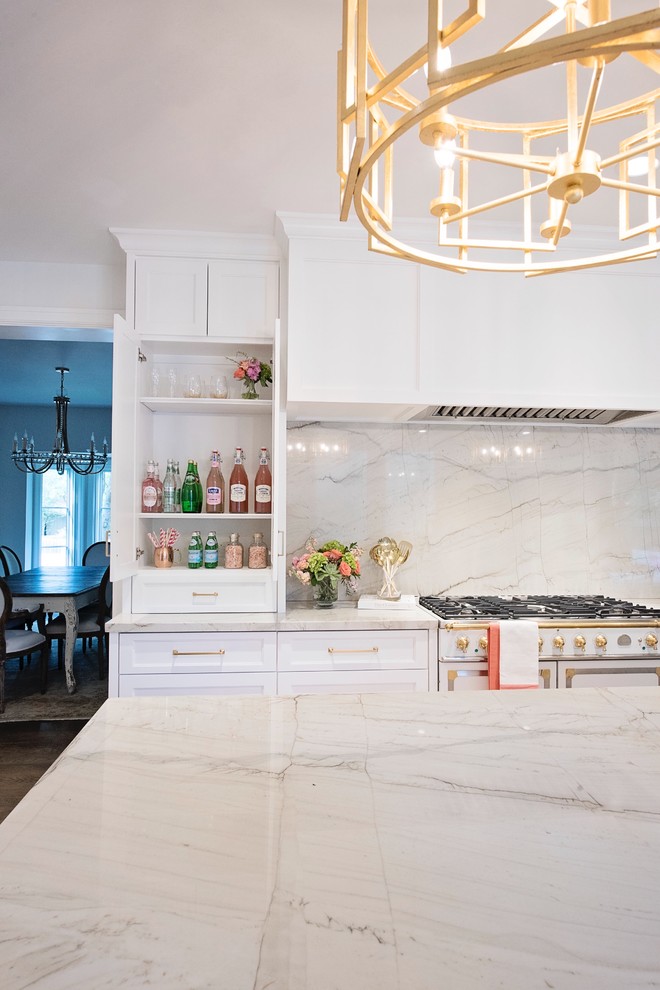 Example of a large transitional l-shaped medium tone wood floor and brown floor open concept kitchen design with a farmhouse sink, recessed-panel cabinets, white cabinets, quartzite countertops, white backsplash, stone slab backsplash, paneled appliances and an island