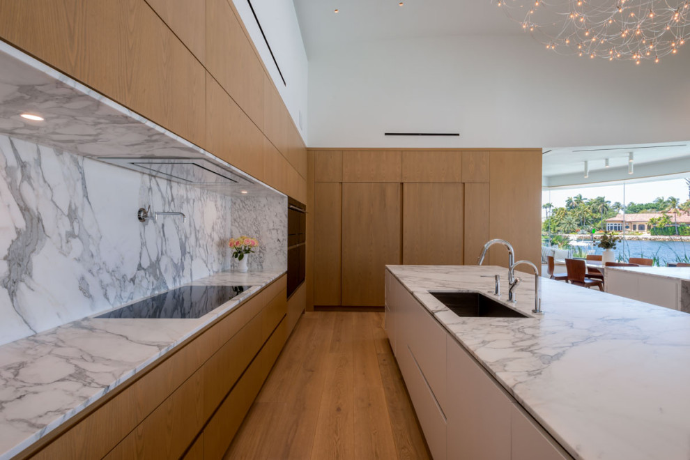 Cette image montre une grande cuisine linéaire minimaliste en bois brun avec un placard à porte plane, plan de travail en marbre, une crédence en marbre, un sol en bois brun et 2 îlots.