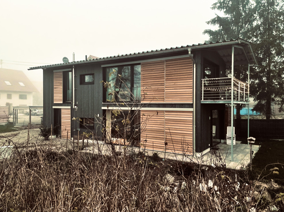 Small contemporary two-storey black house exterior in Munich with wood siding, a gable roof, a metal roof, a grey roof and clapboard siding.