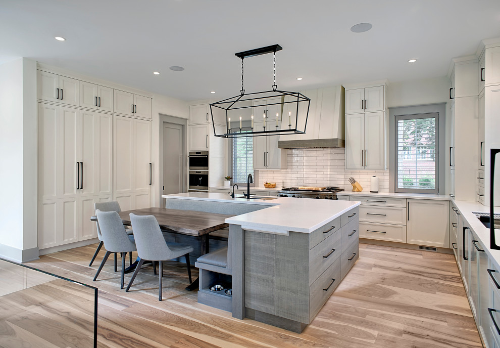 Photo of a large transitional u-shaped open plan kitchen in Chicago with an undermount sink, shaker cabinets, white cabinets, quartzite benchtops, white splashback, ceramic splashback, stainless steel appliances, medium hardwood floors, with island, brown floor and white benchtop.