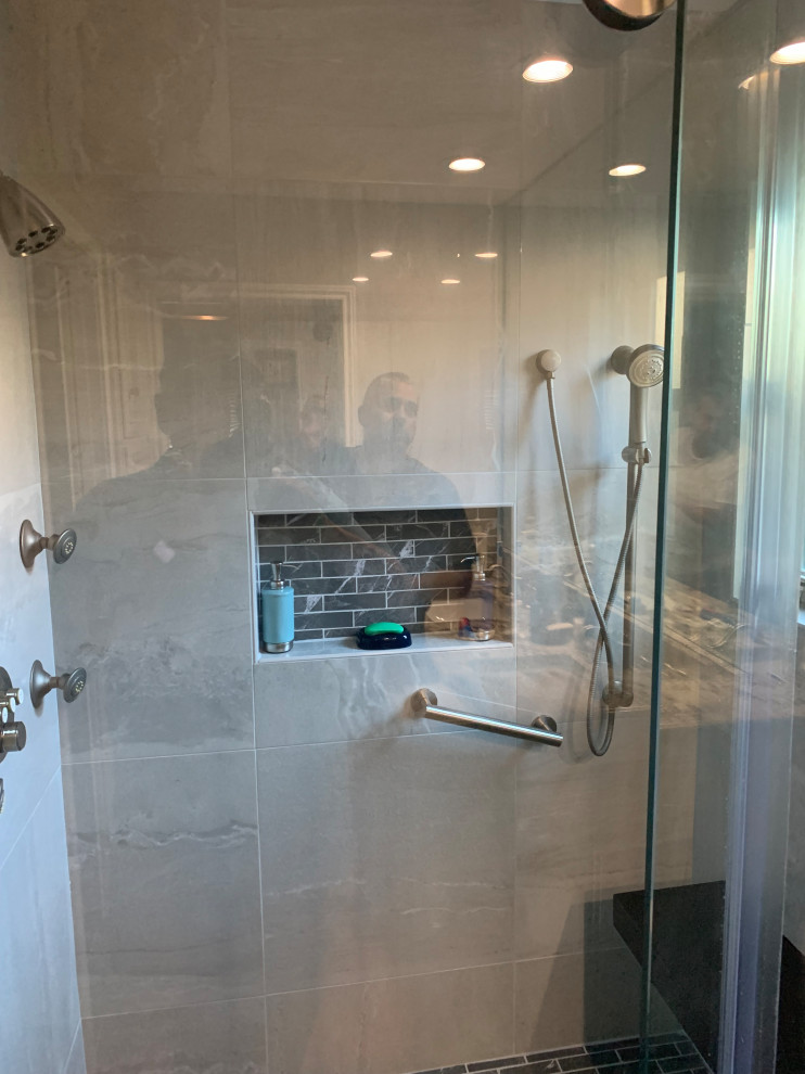 Design ideas for a mid-sized transitional master bathroom in Austin with a curbless shower, gray tile, porcelain tile, grey walls, porcelain floors, brown floor, a sliding shower screen, a shower seat, a built-in vanity and decorative wall panelling.