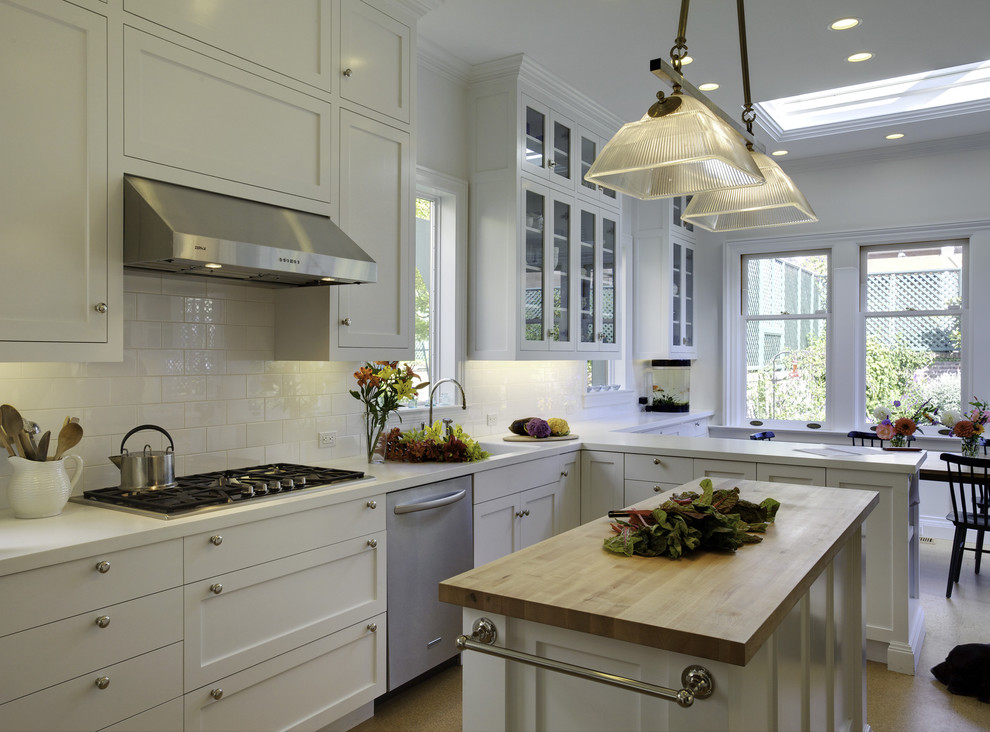 Photo of a mid-sized traditional l-shaped eat-in kitchen in San Francisco with stainless steel appliances, subway tile splashback, white cabinets, solid surface benchtops, white splashback, with island, a drop-in sink, shaker cabinets and cork floors.