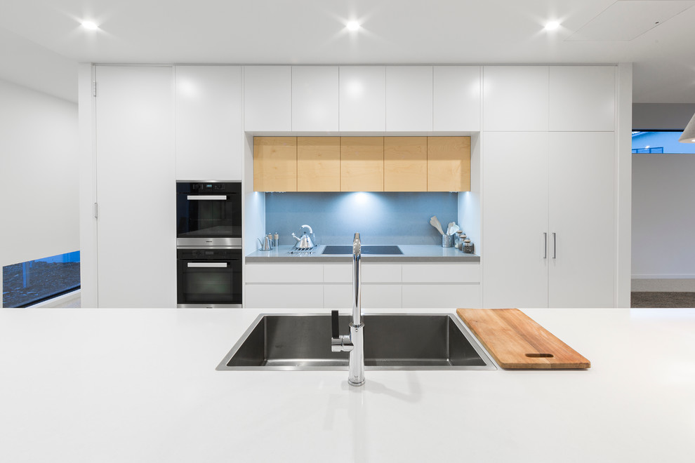 Inspiration for a large contemporary galley kitchen pantry in Canberra - Queanbeyan with an undermount sink, flat-panel cabinets, white cabinets, solid surface benchtops, blue splashback, glass sheet splashback, stainless steel appliances, terrazzo floors and with island.