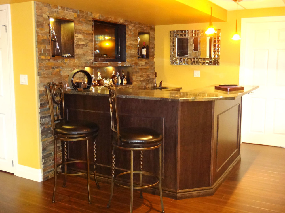 Photo of a large transitional l-shaped seated home bar in Toronto with an undermount sink, brown cabinets, granite benchtops, multi-coloured splashback, stone slab splashback, multi-coloured benchtop, laminate floors and brown floor.