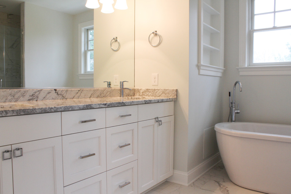 This is an example of a mid-sized traditional master bathroom in DC Metro with recessed-panel cabinets, white cabinets, a freestanding tub, an alcove shower, white tile, marble, grey walls, marble floors, an undermount sink, marble benchtops, white floor, a hinged shower door, multi-coloured benchtops and a two-piece toilet.