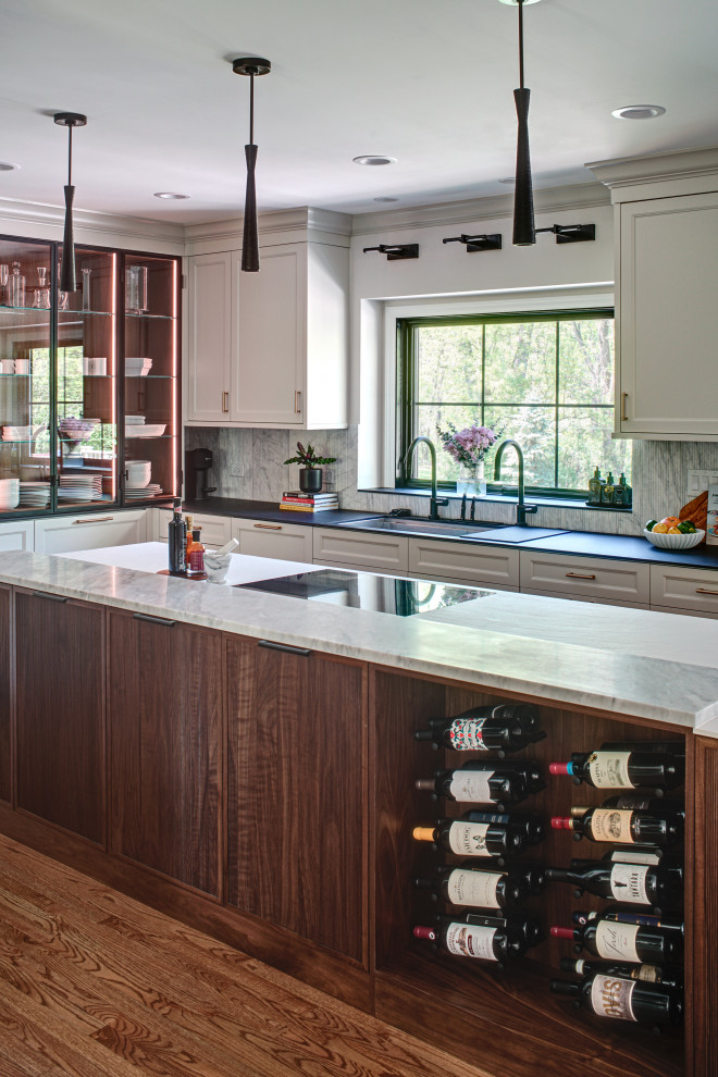 Example of a large transitional l-shaped medium tone wood floor and brown floor eat-in kitchen design in Chicago with an undermount sink, flat-panel cabinets, white cabinets, solid surface countertops, white backsplash, marble backsplash, paneled appliances, an island and black countertops