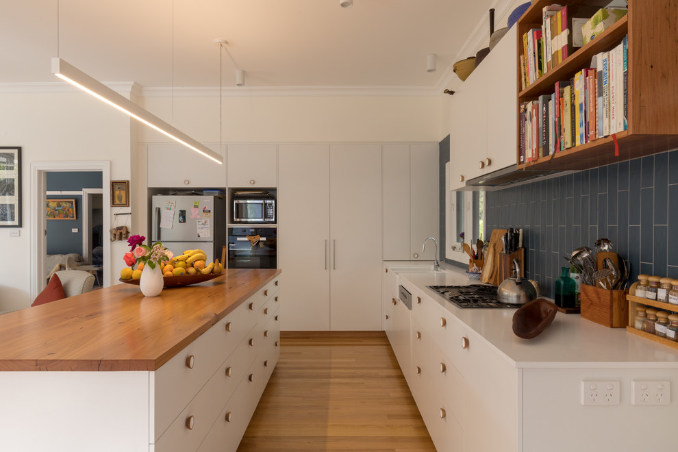 This is an example of a large traditional galley open plan kitchen in Canberra - Queanbeyan with a farmhouse sink, white cabinets, quartz benchtops, blue splashback, ceramic splashback, stainless steel appliances, medium hardwood floors, with island, yellow floor and white benchtop.
