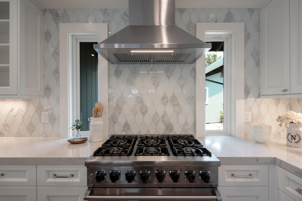 Bild på ett stort funkis vit vitt kök, med en undermonterad diskho, skåp i shakerstil, vita skåp, bänkskiva i kvarts, blått stänkskydd, stänkskydd i glaskakel, rostfria vitvaror, vinylgolv, en köksö och brunt golv