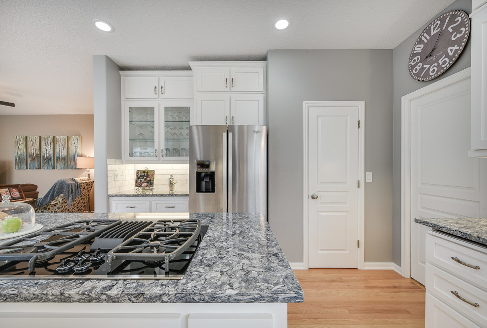 Enclosed kitchen - mid-sized transitional l-shaped light wood floor and brown floor enclosed kitchen idea in Portland with a drop-in sink, shaker cabinets, white cabinets, quartz countertops, white backsplash, subway tile backsplash, an island and stainless steel appliances