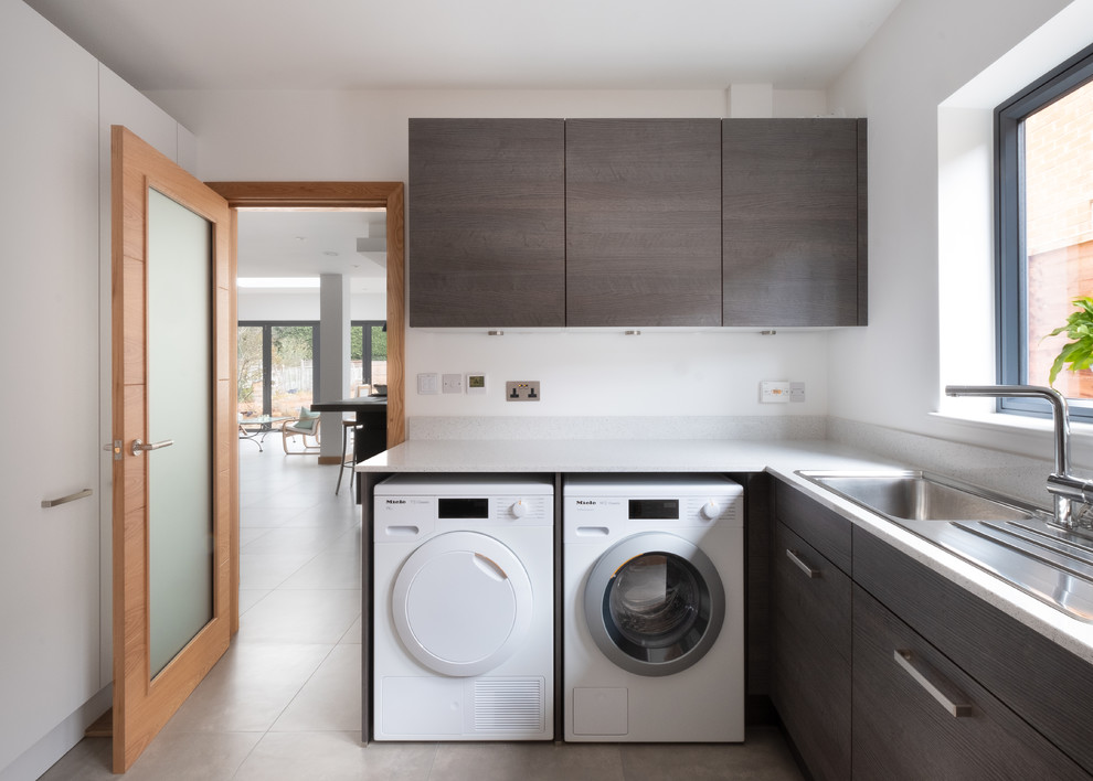 Photo of a large contemporary galley laundry room in Gloucestershire with an integrated sink, flat-panel cabinets, quartzite benchtops, blue splashback, glass sheet splashback, porcelain floors, grey floor and white benchtop.