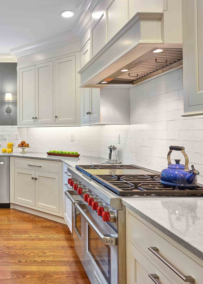 This is an example of a large transitional l-shaped eat-in kitchen in Bridgeport with a drop-in sink, beaded inset cabinets, white cabinets, limestone benchtops, white splashback, ceramic splashback, stainless steel appliances, medium hardwood floors, with island, brown floor and grey benchtop.