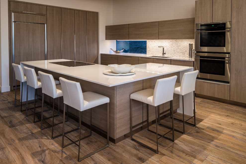Photo of a contemporary l-shaped kitchen in Other with medium wood cabinets, white splashback, stainless steel appliances, medium hardwood floors, with island and brown floor.
