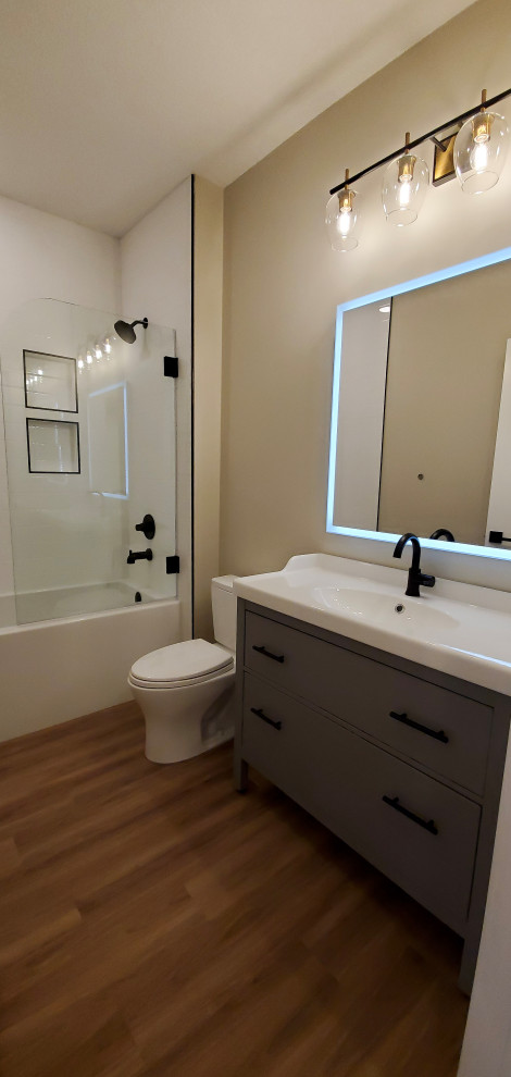 Photo of a medium sized farmhouse shower room bathroom in Edmonton with flat-panel cabinets, green cabinets, an alcove bath, a shower/bath combination, a two-piece toilet, white tiles, beige walls, vinyl flooring, an integrated sink, brown floors, an open shower, white worktops, a wall niche, a single sink and a freestanding vanity unit.