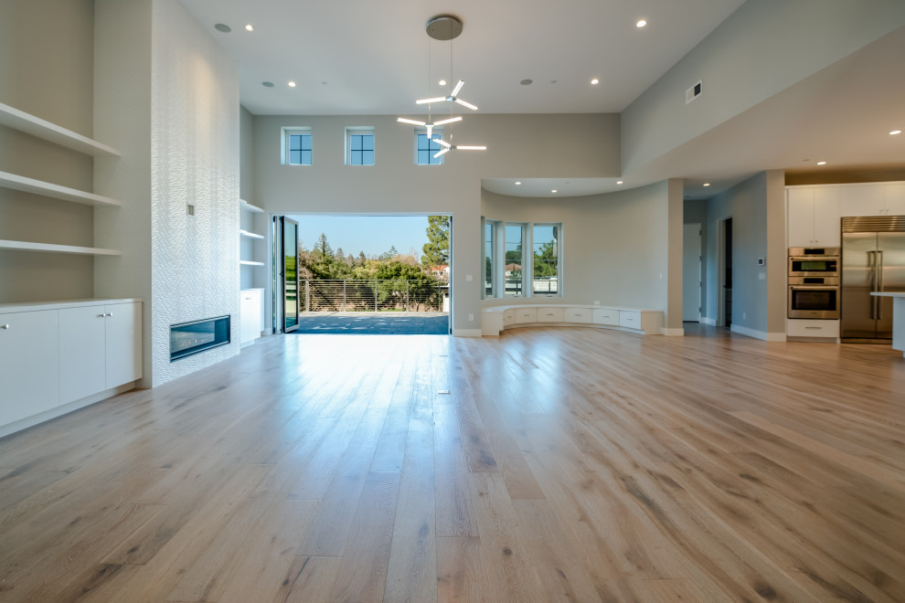 This is an example of a large transitional formal open concept living room in San Francisco with grey walls, light hardwood floors, a standard fireplace, a tile fireplace surround, a built-in media wall and white floor.