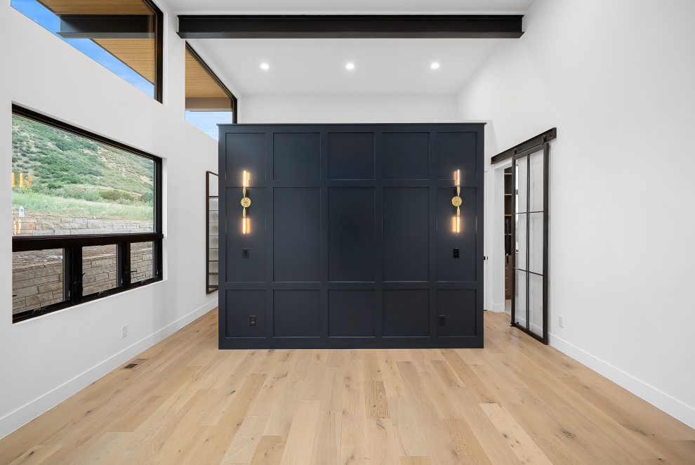 Inspiration for a large midcentury master bedroom in Denver with black walls, light hardwood floors, a two-sided fireplace, a stone fireplace surround, brown floor and exposed beam.