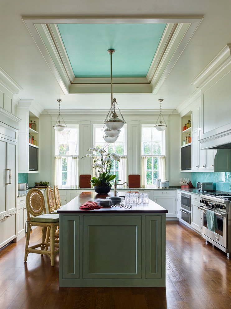Inspiration for a traditional u-shaped kitchen in New York with recessed-panel cabinets, white cabinets, green splashback, stainless steel appliances, medium hardwood floors, with island, brown floor and brown benchtop.