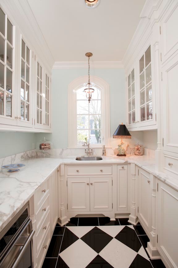 Design ideas for a small traditional galley kitchen pantry in Indianapolis with a farmhouse sink, flat-panel cabinets, white cabinets, marble benchtops, white splashback, subway tile splashback, stainless steel appliances, ceramic floors, black floor and white benchtop.