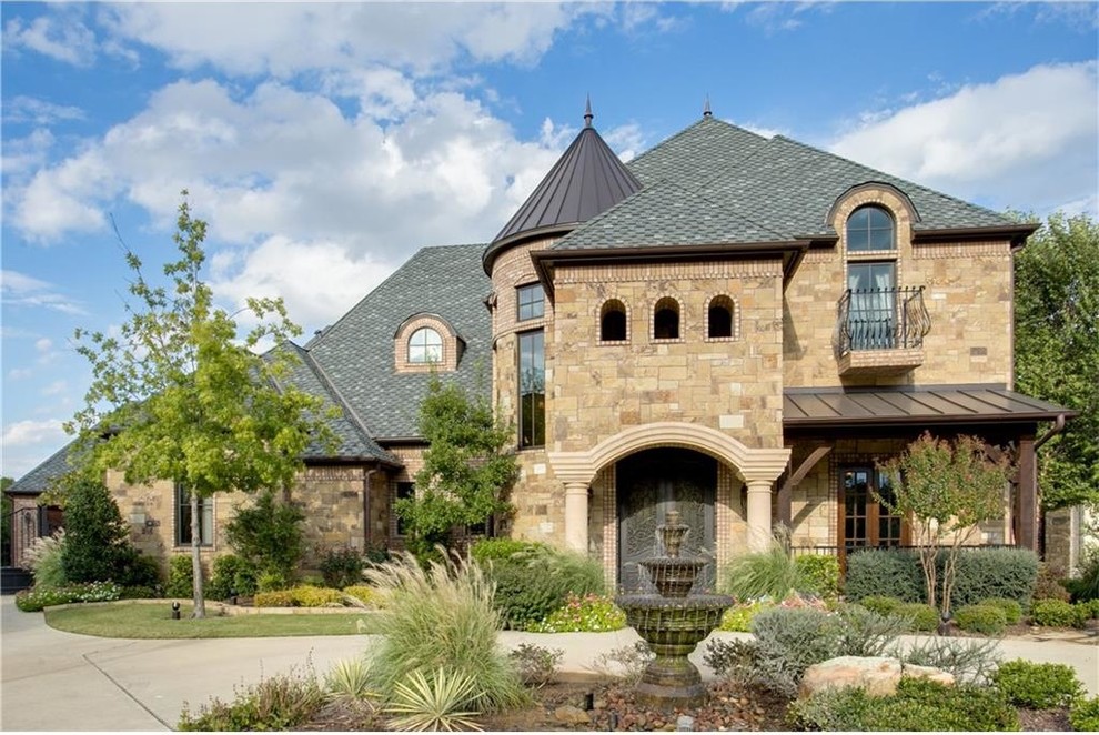 This is an example of a large traditional two-storey beige house exterior in Dallas with stone veneer, a mixed roof and a hip roof.