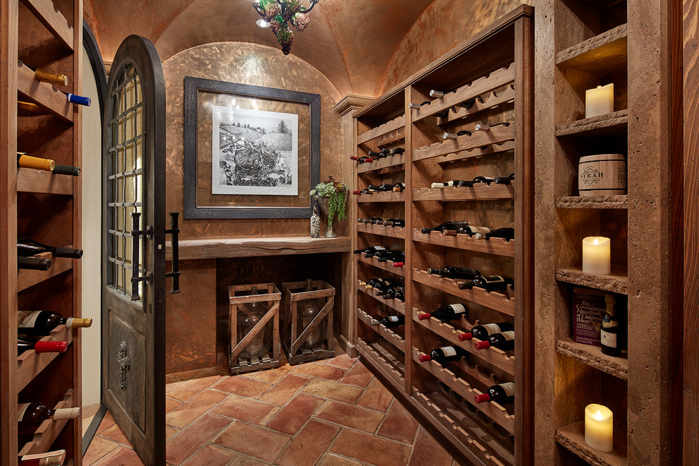 This is an example of a large country wine cellar in Orange County with terra-cotta floors, storage racks and brown floor.