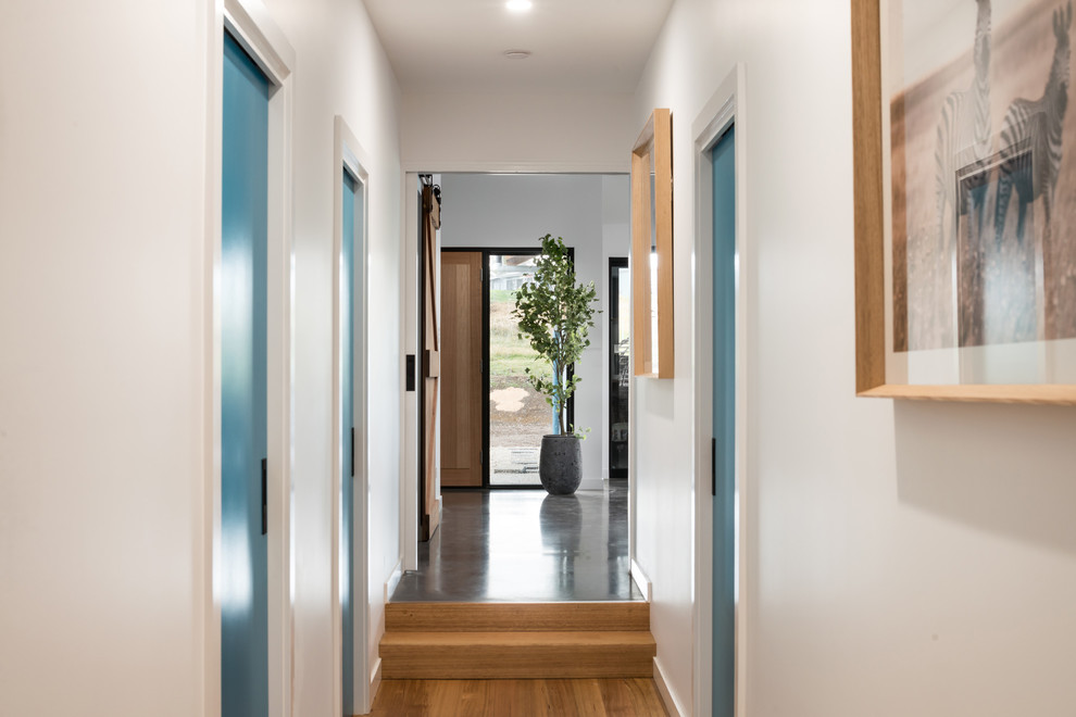 This is an example of a mid-sized contemporary hallway in Hobart with white walls, light hardwood floors and brown floor.