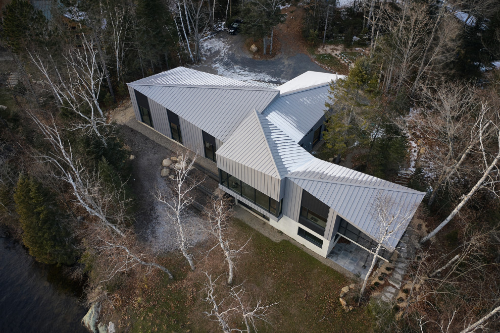 Réalisation d'une grande façade de maison métallique et grise design en bardage à clin à un étage avec un toit à croupette, un toit en métal et un toit gris.