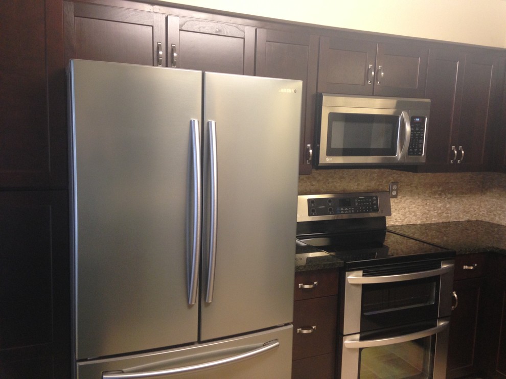 Example of a mid-sized transitional l-shaped porcelain tile enclosed kitchen design with an undermount sink, shaker cabinets, dark wood cabinets, granite countertops, beige backsplash, stone tile backsplash, stainless steel appliances and an island