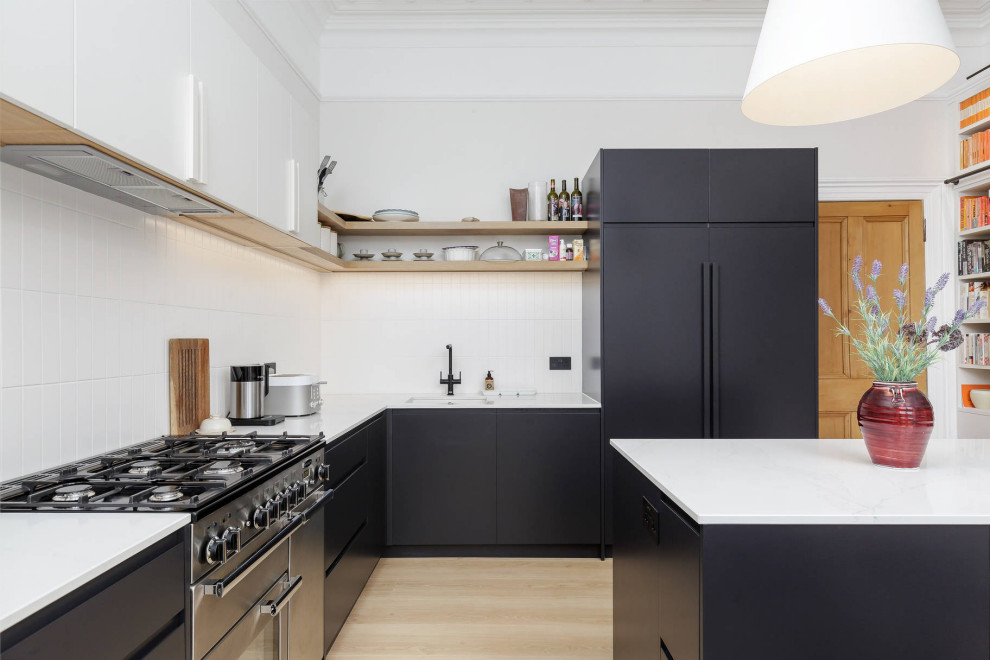 Inspiration for a mid-sized contemporary l-shaped eat-in kitchen in Edinburgh with quartz benchtops, white splashback, ceramic splashback, laminate floors, with island, white benchtop, black cabinets, panelled appliances, beige floor and coffered.