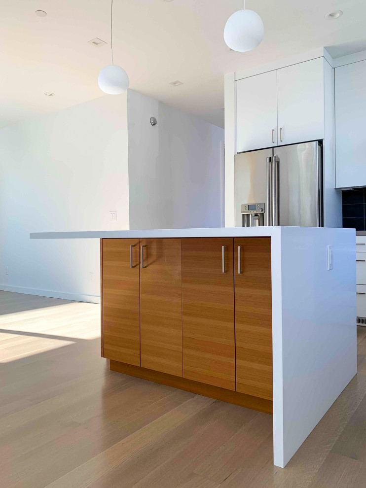 Contemporary open plan kitchen in San Francisco with an undermount sink, flat-panel cabinets, white cabinets, black splashback, ceramic splashback, stainless steel appliances, light hardwood floors, with island, brown floor and white benchtop.