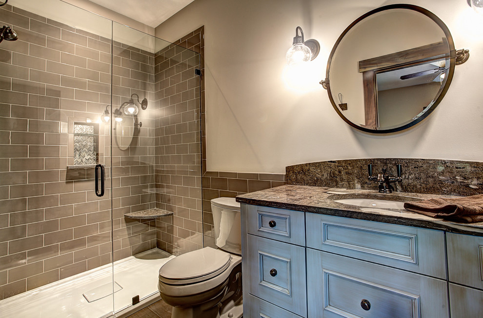 Photo of a country bathroom in Other with recessed-panel cabinets, blue cabinets, an alcove shower, a two-piece toilet, brown tile, subway tile, white walls, an undermount sink and a hinged shower door.