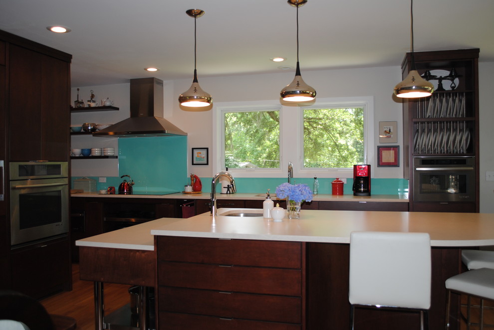 Photo of a mid-sized midcentury l-shaped kitchen in Atlanta with a single-bowl sink, flat-panel cabinets, dark wood cabinets, glass benchtops, glass sheet splashback, stainless steel appliances, light hardwood floors and with island.