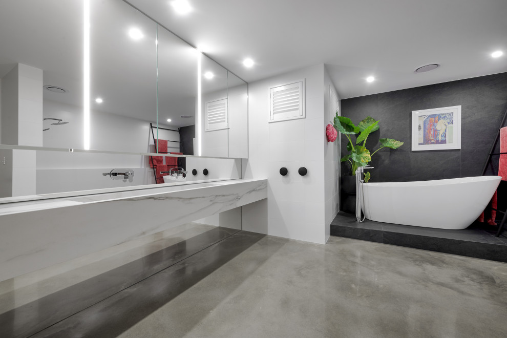 Photo of a large contemporary master bathroom in Perth with white cabinets, a freestanding tub, concrete floors, grey floor, white benchtops, a floating vanity, gray tile, white walls, a trough sink and a double vanity.