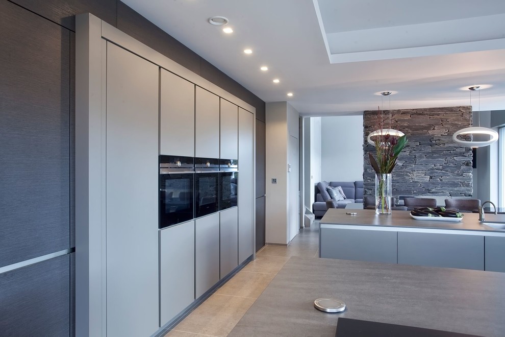This is an example of a large modern single-wall open plan kitchen in Belfast with a drop-in sink, flat-panel cabinets, beige cabinets, quartz benchtops, stainless steel appliances, ceramic floors, multiple islands and beige floor.