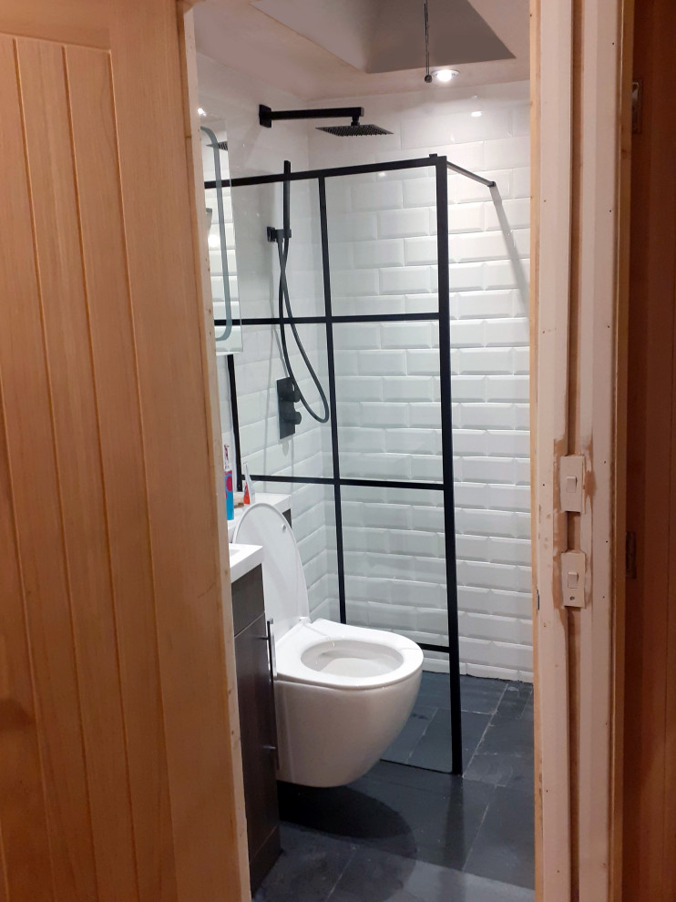 This is an example of a small modern 3/4 bathroom in Cornwall with flat-panel cabinets, dark wood cabinets, an open shower, a wall-mount toilet, white tile, subway tile, white walls, slate floors, an integrated sink, solid surface benchtops, black floor, an open shower, white benchtops, a single vanity and a built-in vanity.