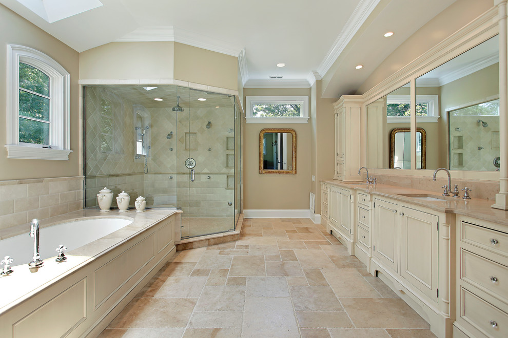 Design ideas for a large transitional master bathroom in Toronto with a corner shower, shaker cabinets, beige cabinets, a drop-in tub, beige walls, limestone floors, an undermount sink, limestone benchtops, beige floor and a hinged shower door.