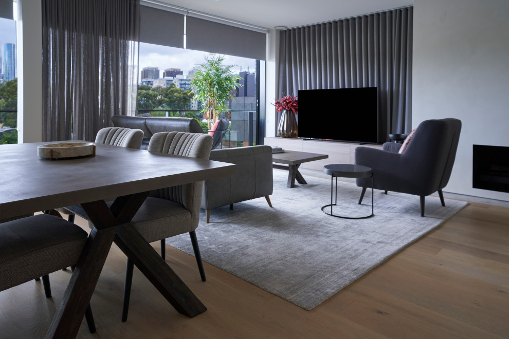 This is an example of a mid-sized contemporary loft-style family room in Melbourne with medium hardwood floors, a standard fireplace, a concrete fireplace surround and a freestanding tv.
