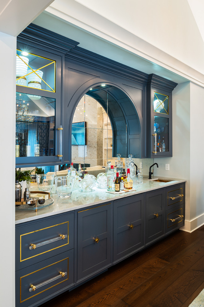 This is an example of a medium sized modern galley wet bar in New York with a built-in sink, recessed-panel cabinets, blue cabinets, engineered stone countertops, multi-coloured splashback, mirror splashback, medium hardwood flooring, brown floors and beige worktops.