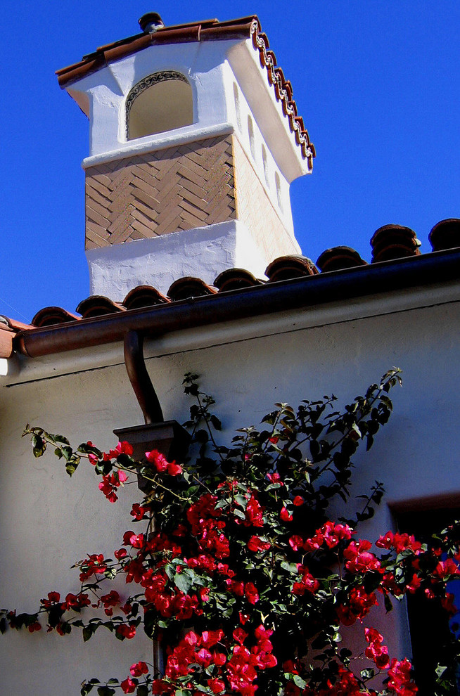 This is an example of a mid-sized mediterranean one-storey stucco white house exterior in Santa Barbara with a clipped gable roof and a tile roof.