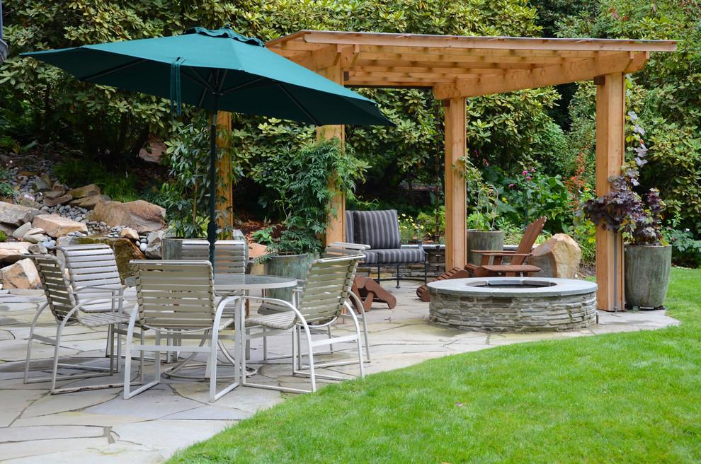 This is an example of a large traditional backyard patio in Seattle with a fire feature, natural stone pavers and a pergola.