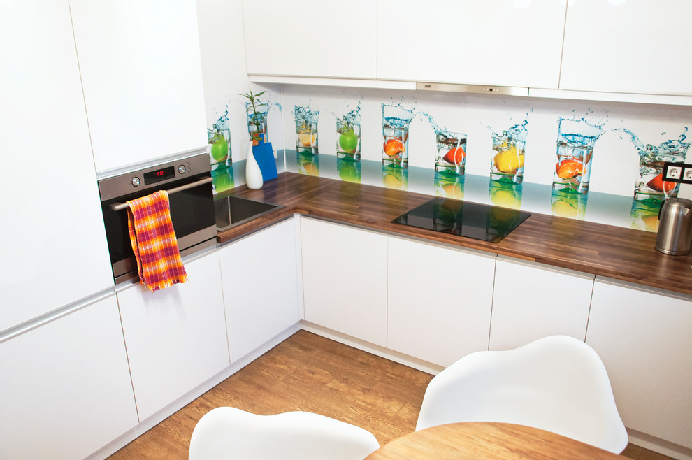 Photo of a small contemporary l-shaped separate kitchen in Moscow with a drop-in sink, flat-panel cabinets, white cabinets, glass sheet splashback, stainless steel appliances, no island, multi-coloured splashback and wood benchtops.