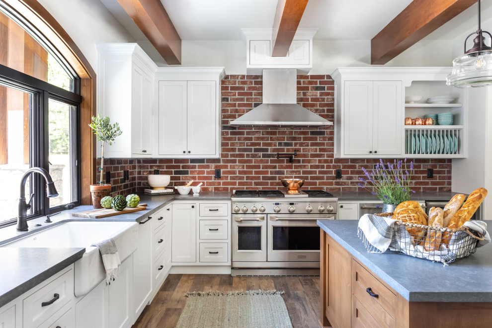 Inspiration for a large transitional u-shaped kitchen pantry in Sacramento with a farmhouse sink, shaker cabinets, white cabinets, quartz benchtops, brown splashback, brick splashback, stainless steel appliances, vinyl floors, with island, brown floor, grey benchtop and exposed beam.