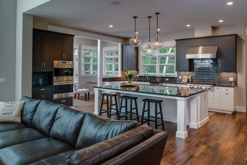 Large transitional single-wall medium tone wood floor open concept kitchen photo with an undermount sink, shaker cabinets, gray cabinets, granite countertops, gray backsplash, ceramic backsplash, stainless steel appliances and an island